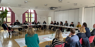 Personen sitzen im großen Saal in einem Kreis und führen eine Diskussion.